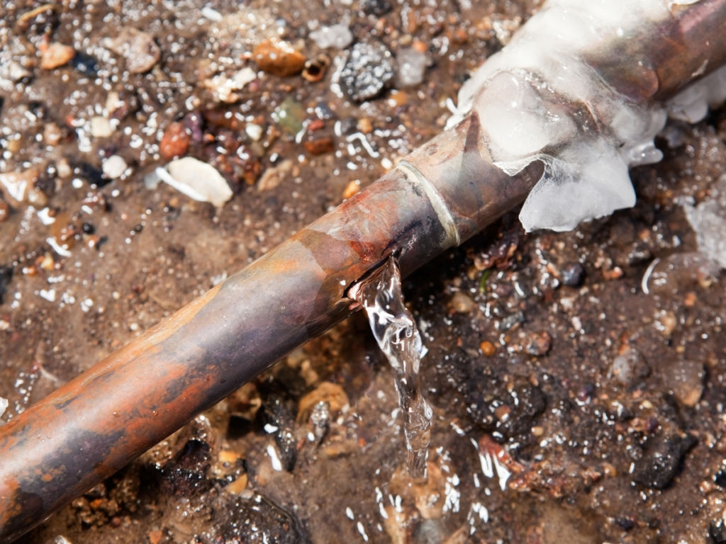 Water leaking from a visible crack in a copper pipe, showing the importance of immediate plumbing repair.