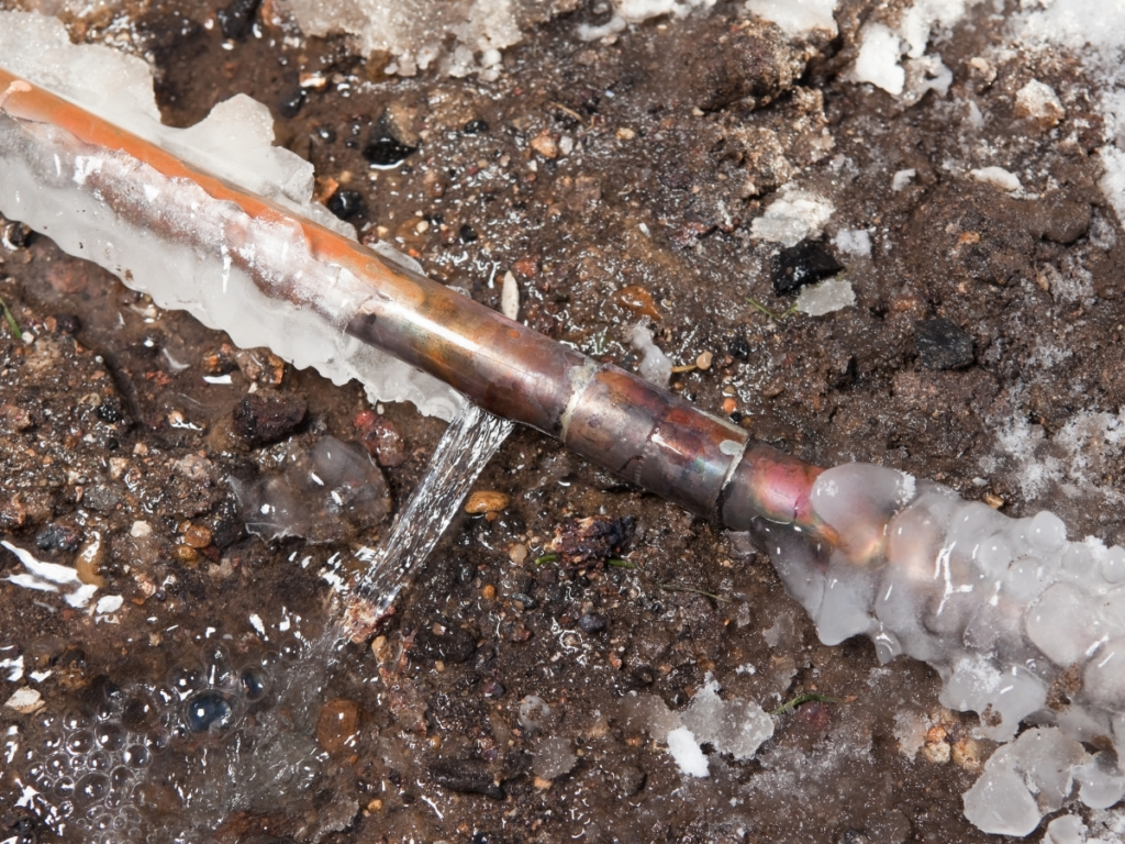 Close-up of a copper water pipe that has burst due to freezing, with ice surrounding the leak.